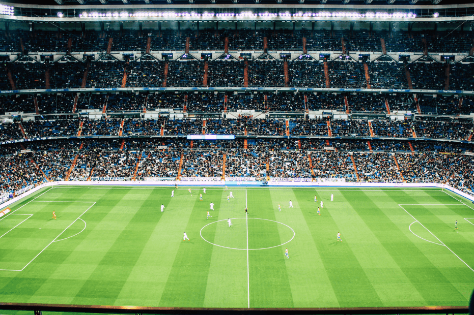 A football stadium, with players on pitch and fans watching the match.