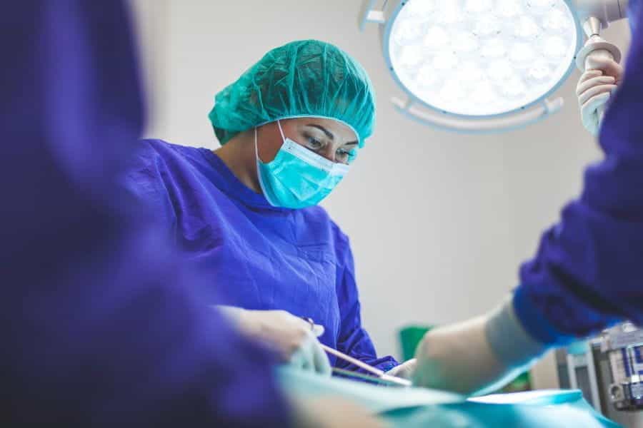 A hospital doctor in blue scrubs and facemask performs an operation.