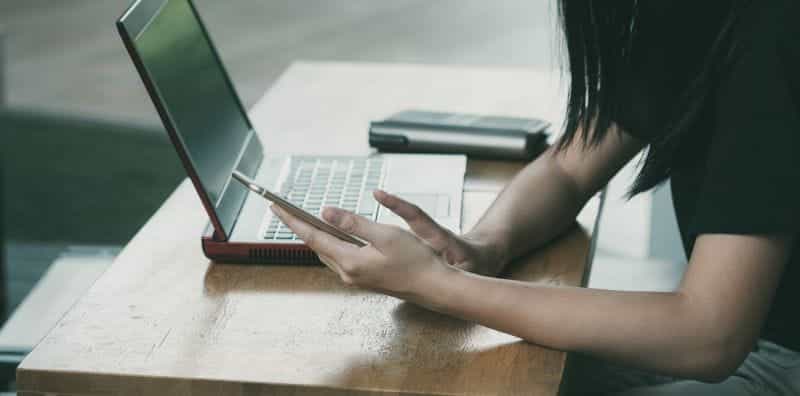 A woman sitting with a laptop, using a mobile phone.