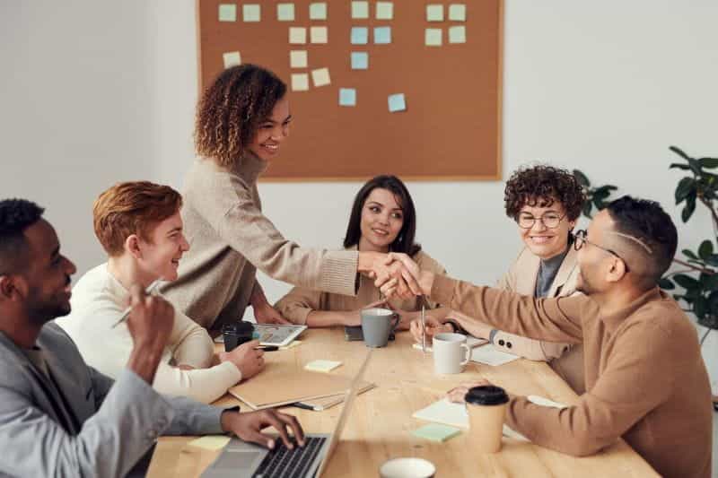A woman shakes hands with a man in an office meeting.