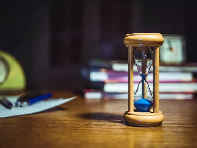 An hourglass timer on a desk with books and pens.