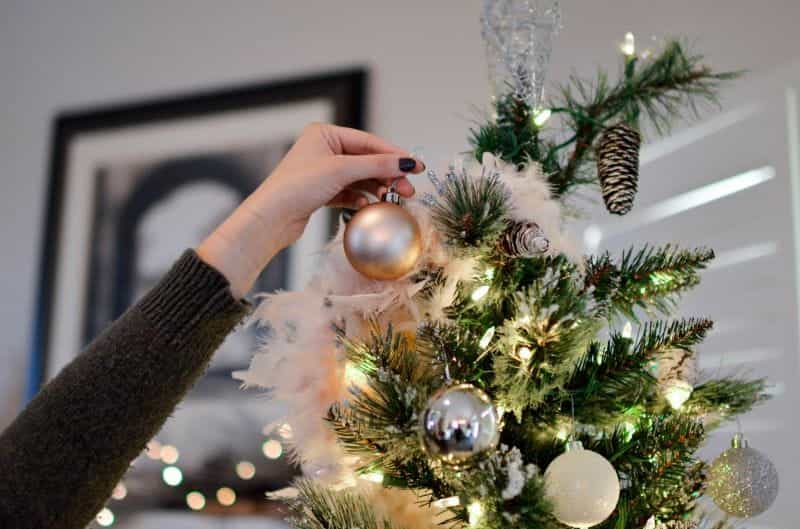 A woman putting a bauble on a Christmas tree decorated with tinsel.