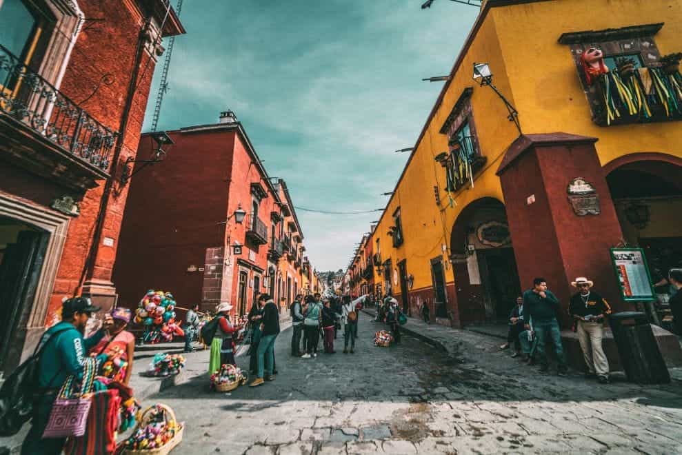 People stand in the street between colorful buildings in San Miguel de Allende, Mexico.