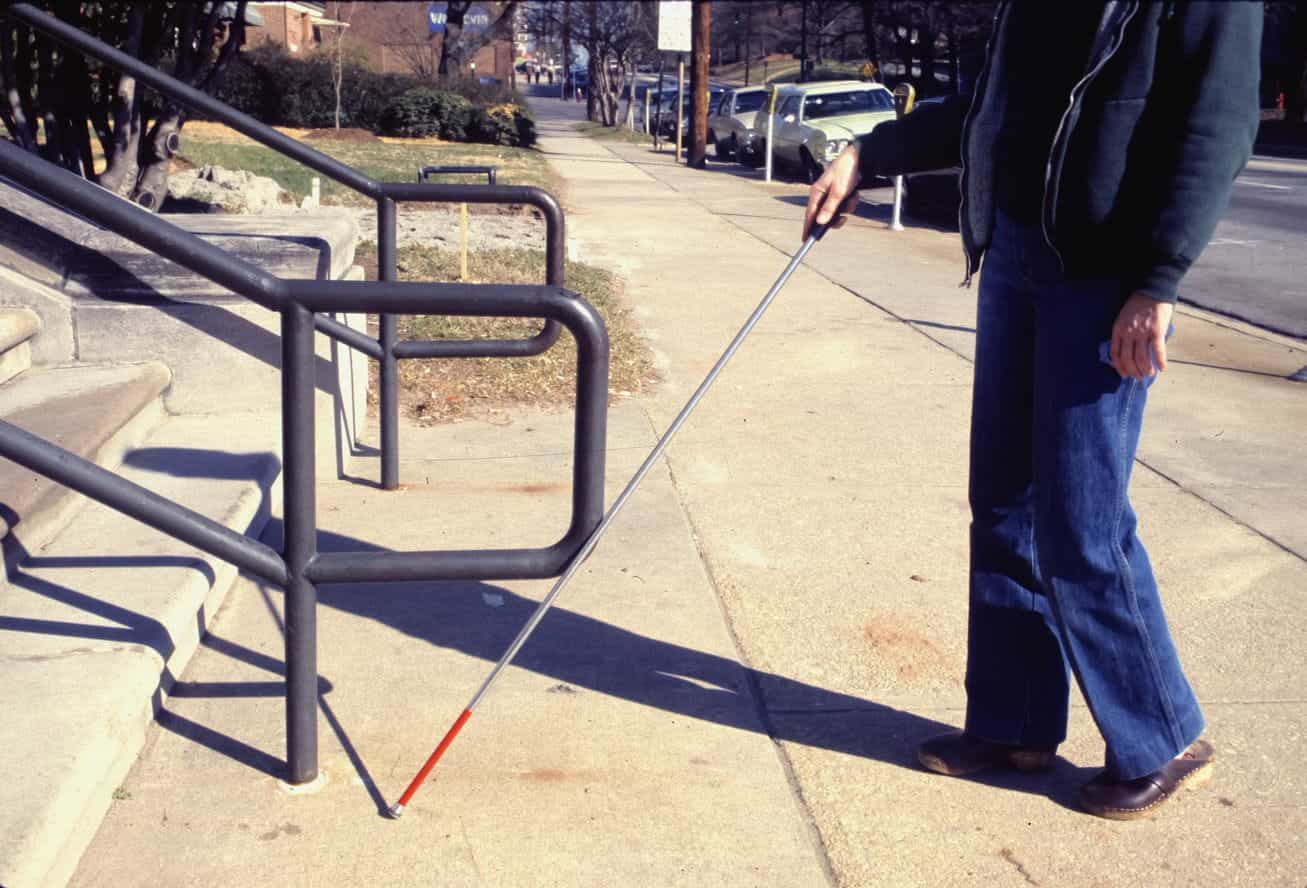 A visually impaired person walks using a cane.