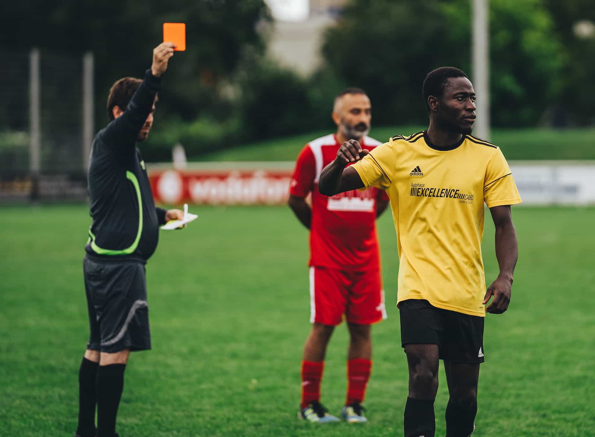 Two soccer players and a ref holding up a red penalty card.