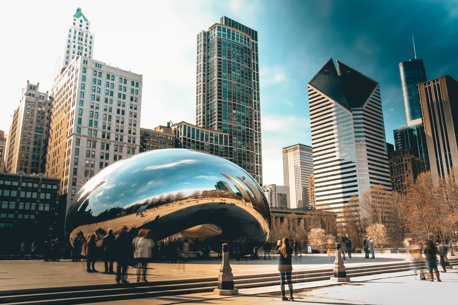The world-famous Bean sculpture in downtown Chicago, Illinois, with countless tall buildings and skyscrapers towering behind it.