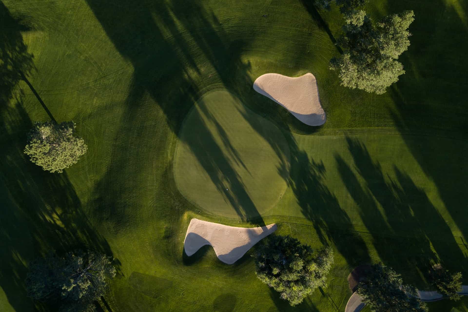 An aerial overhead top-down view of an outdoor golf course, featuring the green around the hole and two sand pits flanking each side of the terrain.