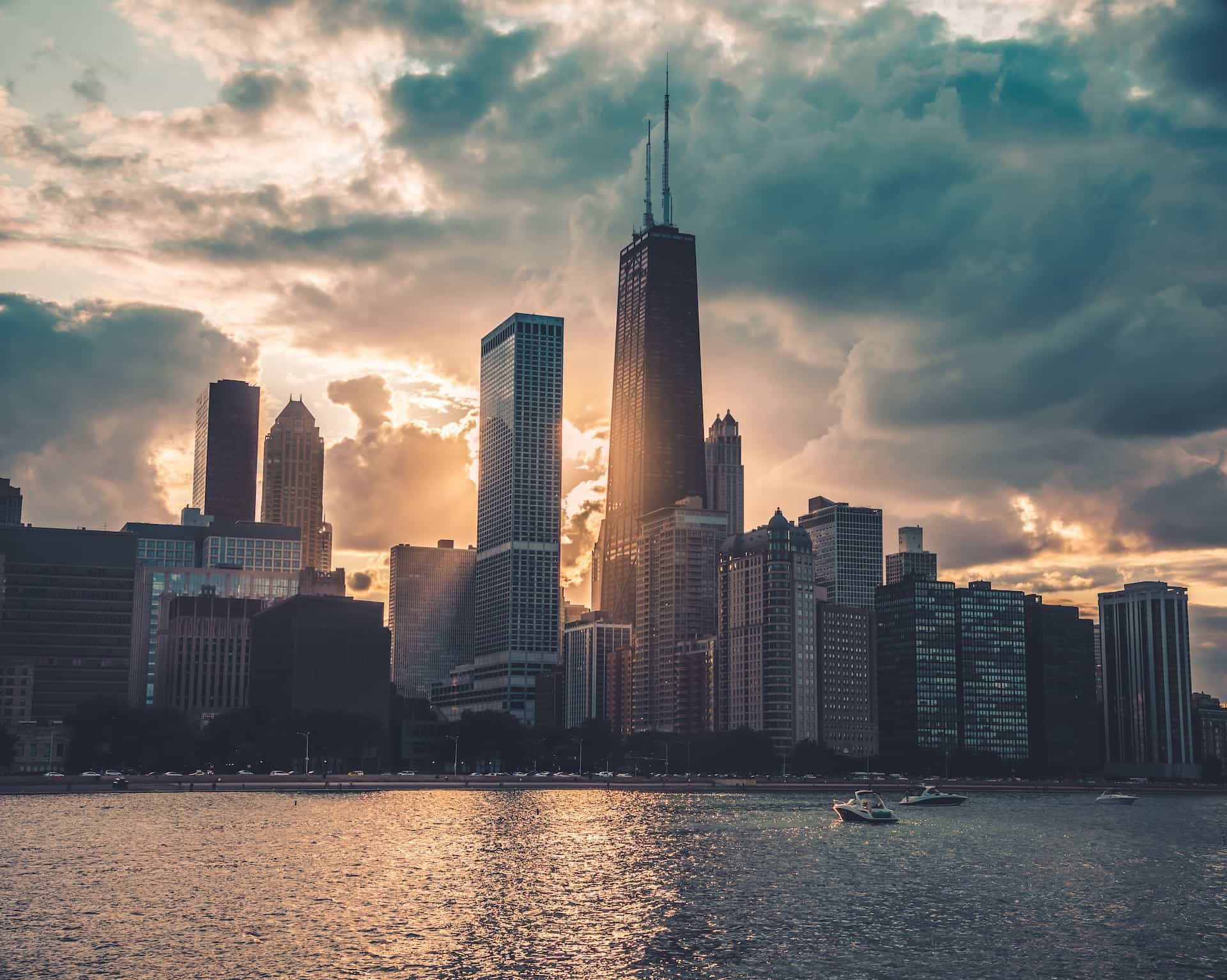 A dense cluster of tall buildings and skyscrapers in the downtown area of Chicago, Illinois, with Lake Michigan’s waters touching up against the waterfront.