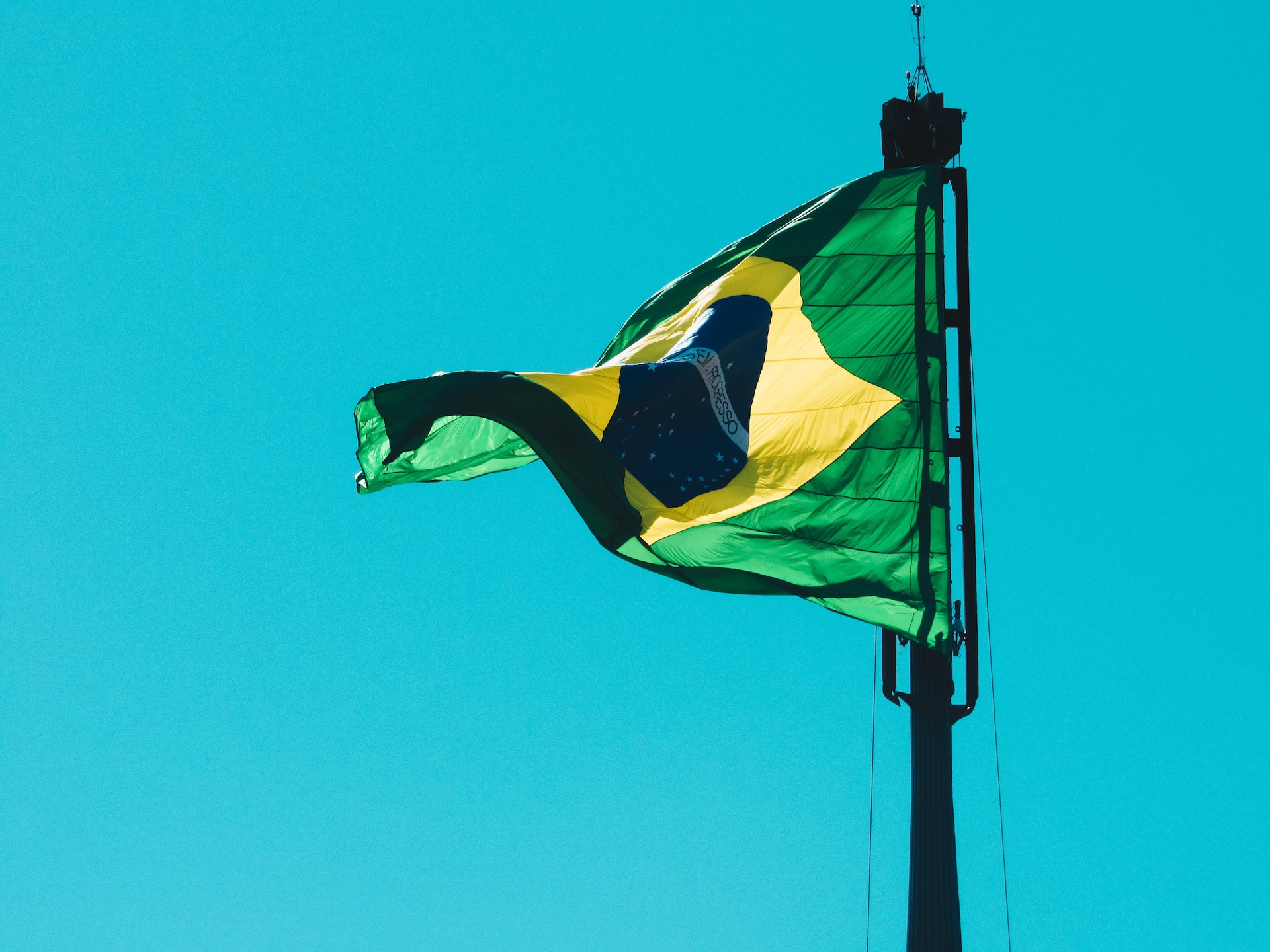 The Brazilian flag waves in the wind against a blue sky.